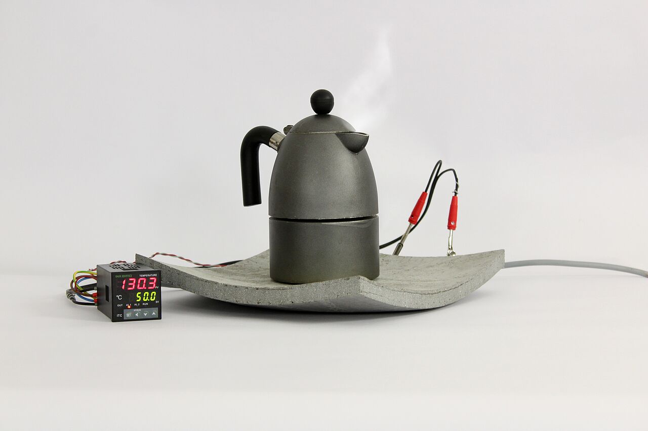 Ein dampfender Espressokocher steht auf einer aufheizbaren, gekrümmten Betonform. Link zur Großansicht des Fotos.