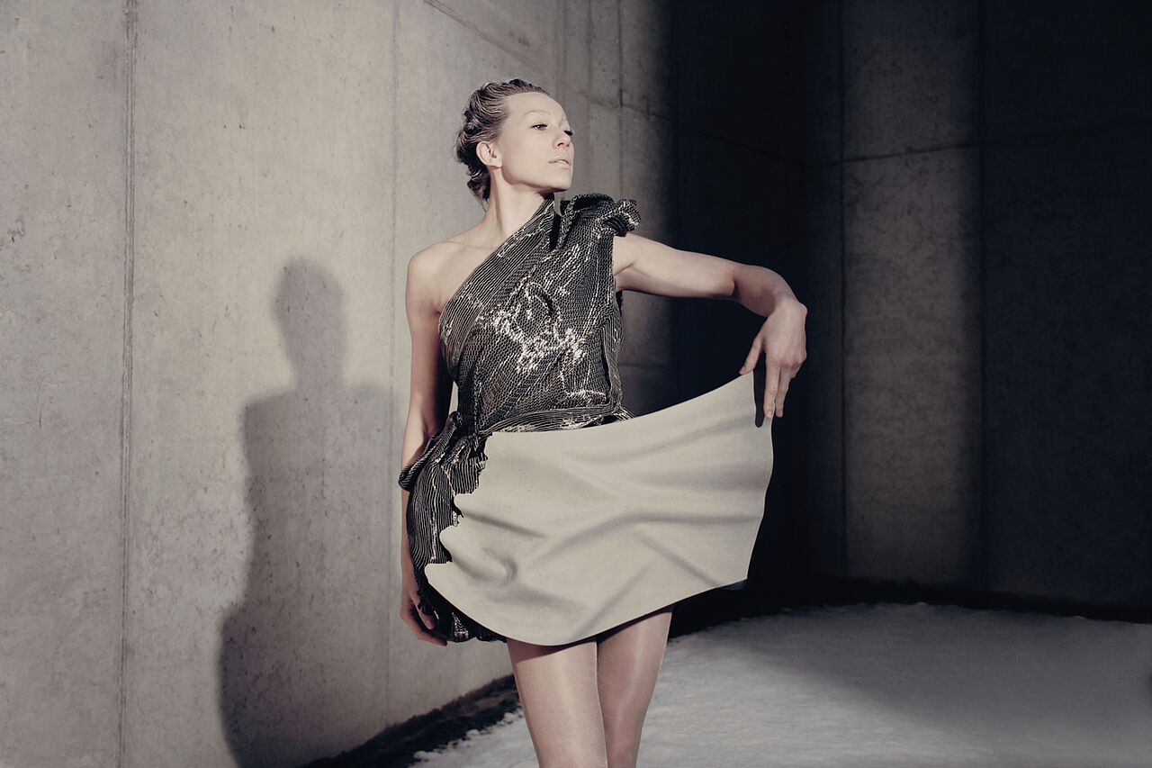 Model steht vor einer Betonwand und trägt ein Kleid aus Carbonbeton. 