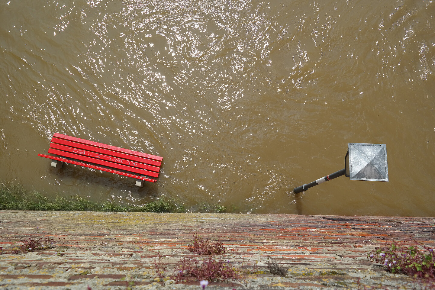 Hochwasser Eine rote Bank und eine Straßenlaterne stehen auf einer überfluteten Straße